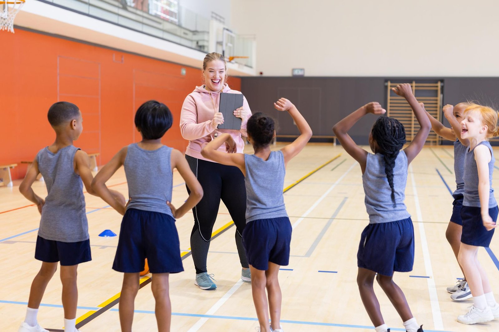 In school gym female coach using tablet to instruct diverse children during fitness class